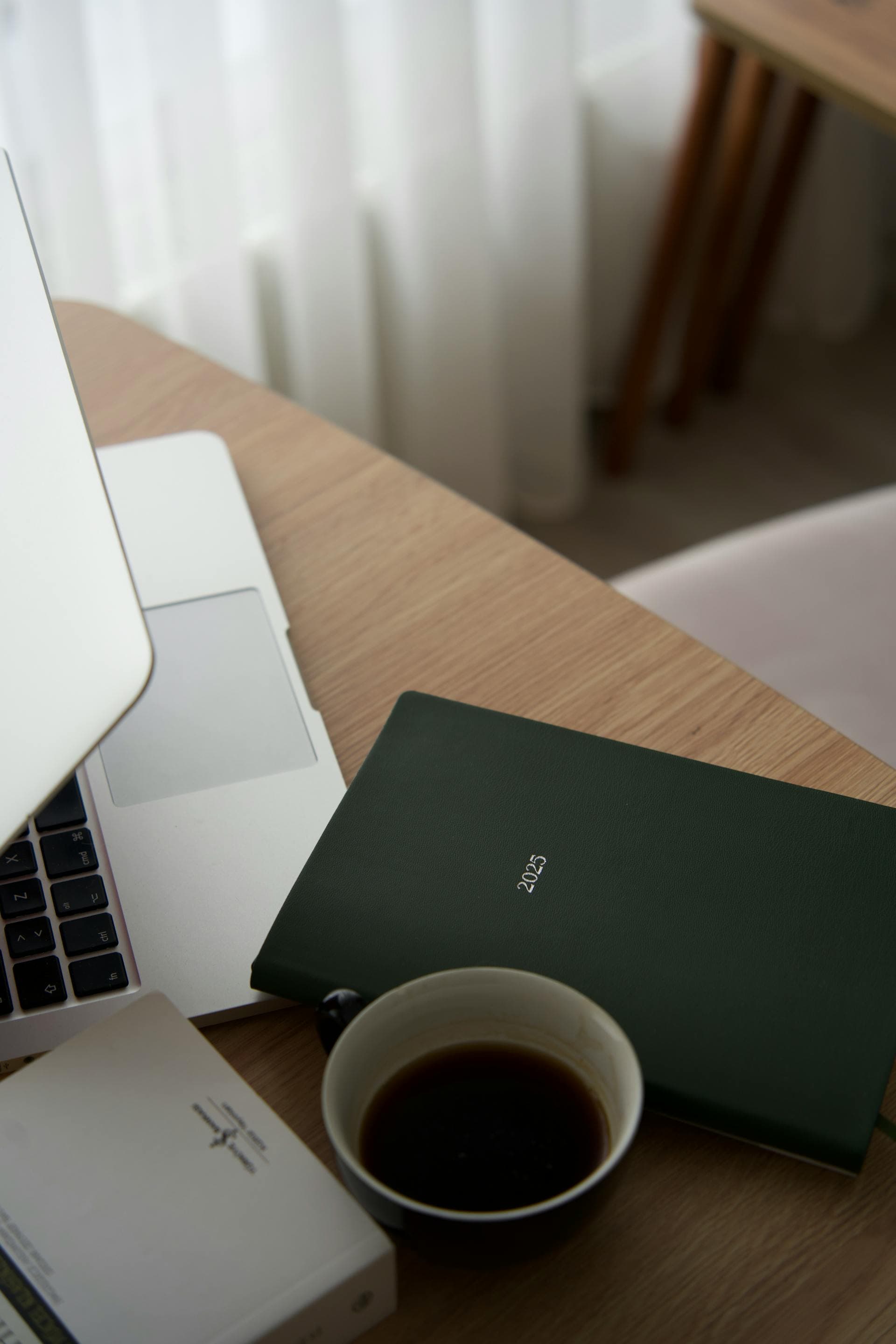 A minimal workspace with a laptop, planner, and coffee cup on a wooden desk
